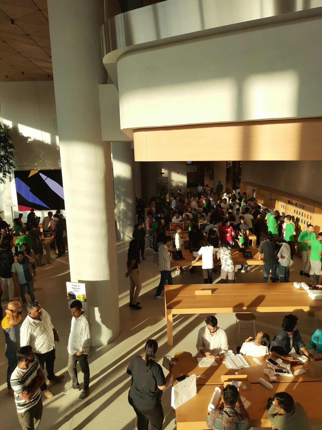Shoppers examine electronics on wooden tables in a busy store.