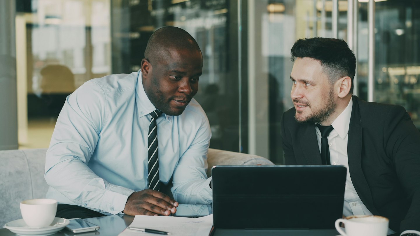 Two businessmen discuss a laptop at a modern office table.